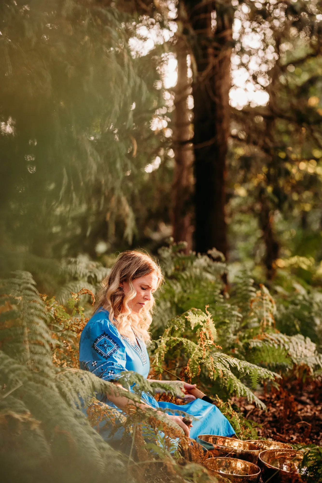 Linsey in blue dress with singing bowls in forest setting