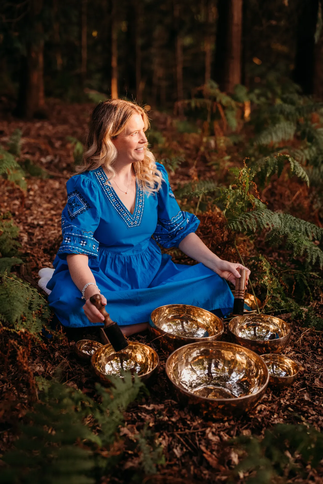 Linsey sitting with multiple singing bowls in natural forest setting